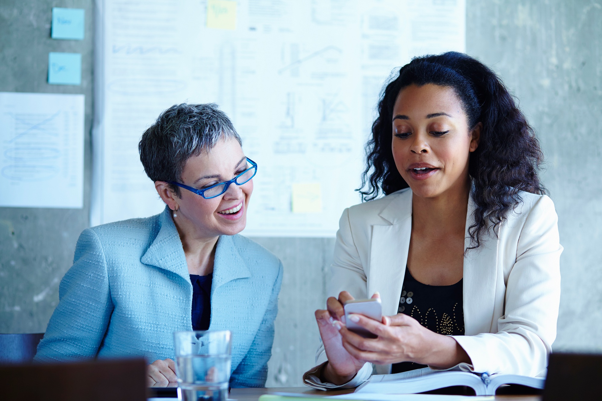 Two professionals engaging in a lively discussion over content on a smartphone in an office setting.